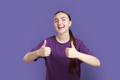 Happy woman showing thumbs up on purple background. Like gesture