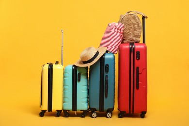 Photo of Many colorful suitcases, beach bags and straw hat on orange background