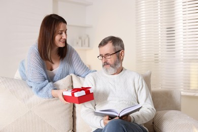 Photo of Happy daughter presenting her father with gift at home