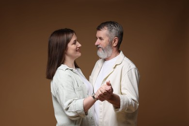 Photo of Happy daughter dancing with her father on brown background