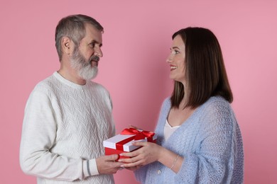 Photo of Happy daughter presenting her father with gift on pink background