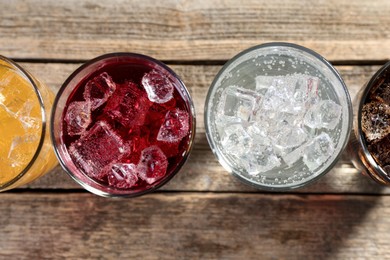 Photo of Soda water of different flavors with ice cubes in glasses on wooden table, flat lay