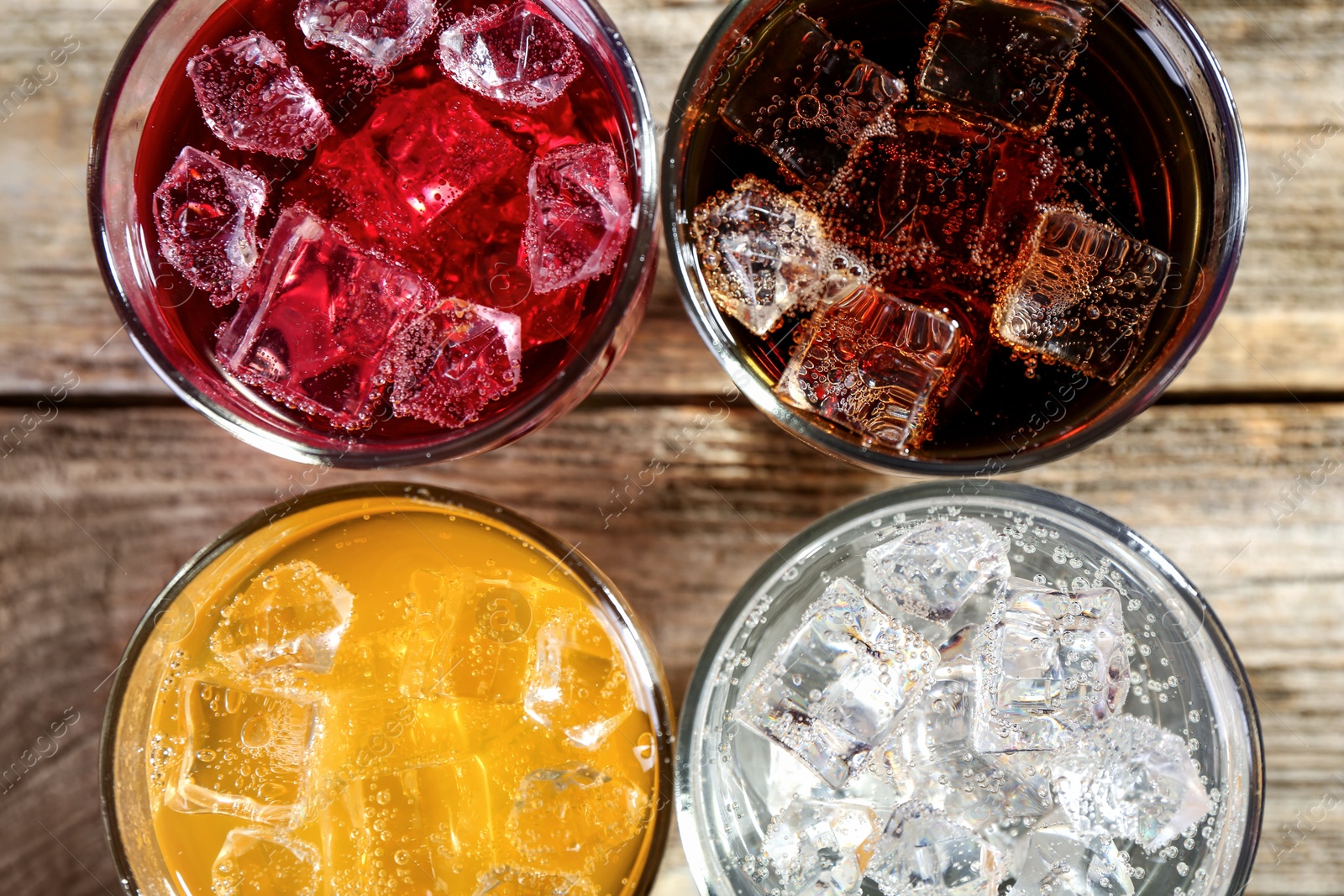 Photo of Soda water of different flavors with ice cubes in glasses on wooden table, flat lay