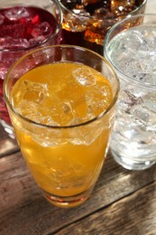 Photo of Soda water of different flavors with ice cubes in glasses on wooden table, closeup