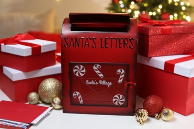 Photo of Santa Claus mailbox, letters, gift boxes and Christmas decor on white table indoors