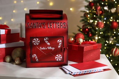 Photo of Santa Claus mailbox, letters, gift boxes and Christmas decor on white table indoors