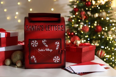 Photo of Santa Claus mailbox, letters, gift boxes and Christmas decor on white table indoors