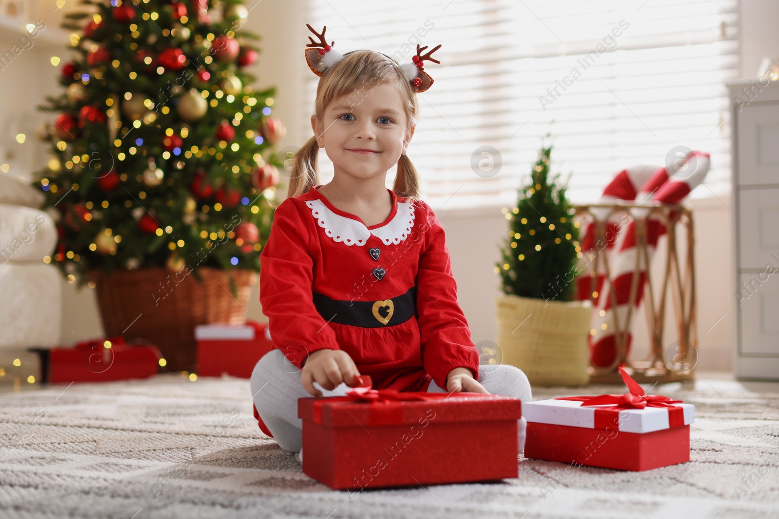 Photo of Little girl in Christmas costume with gift boxes at home