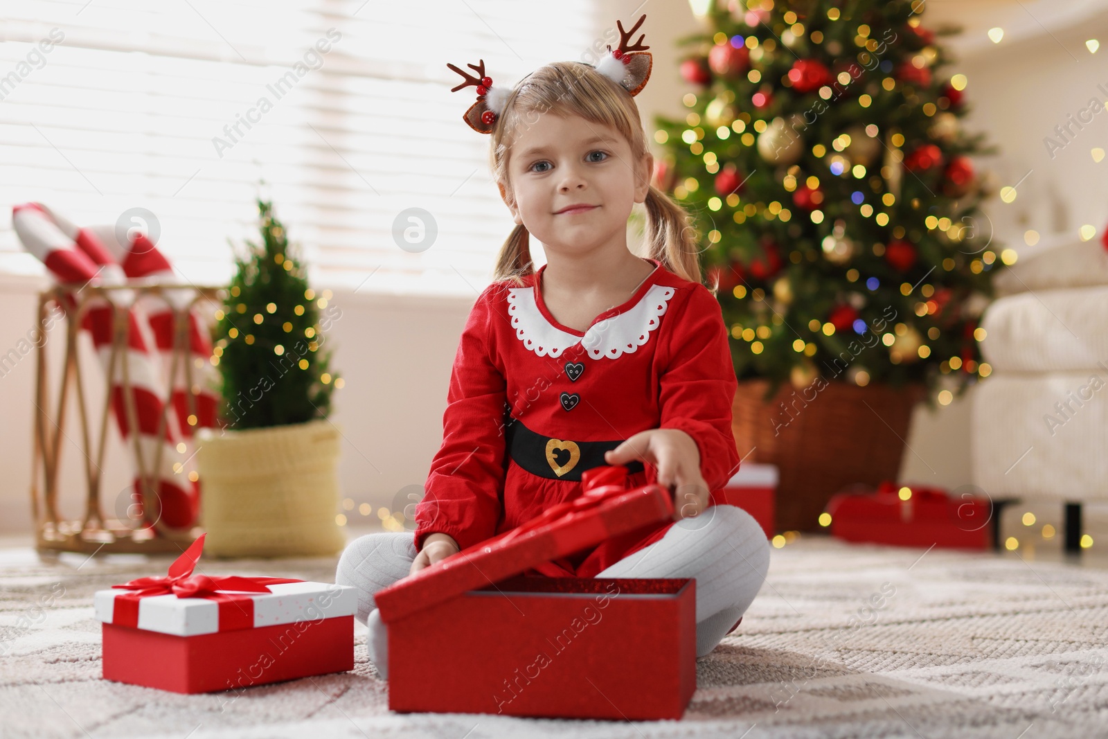 Photo of Little girl in Christmas costume with gift boxes at home