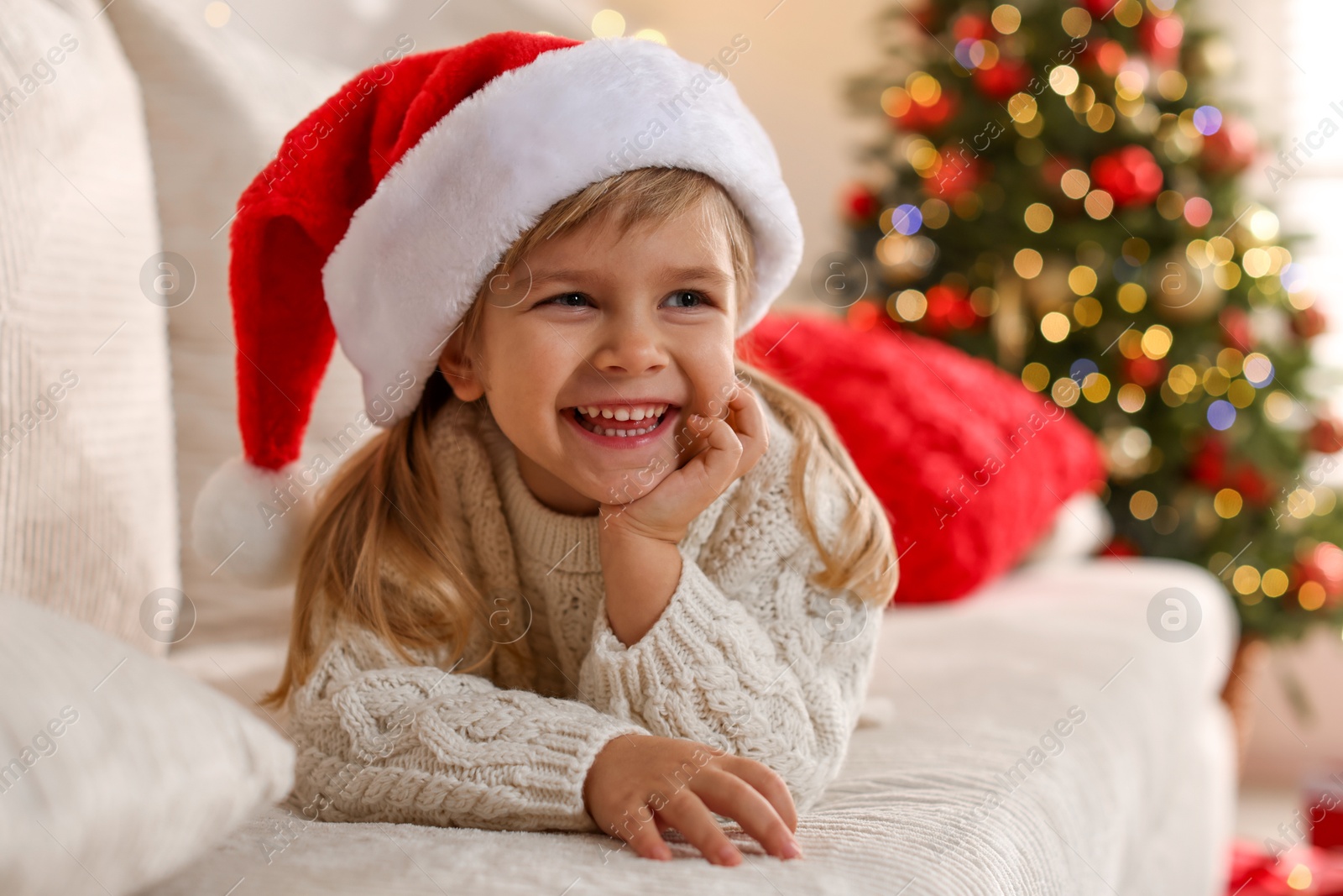 Photo of Little girl in Santa hat lying on sofa at home