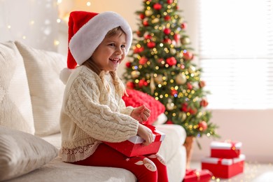 Photo of Little girl in Santa hat sitting on sofa at home