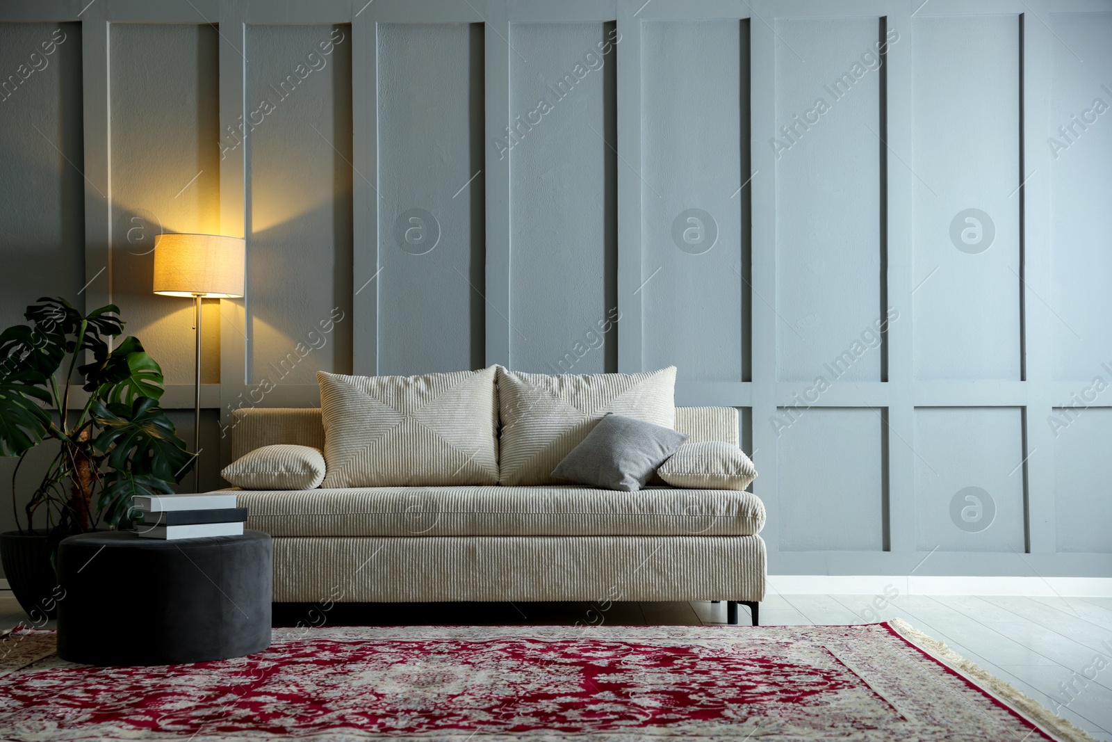 Photo of Comfortable sofa with pillows, lamp, houseplant and pouf near grey wall indoors. Space for text