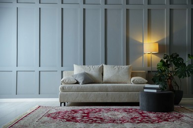 Photo of Comfortable sofa with pillows, lamp, houseplant and pouf near grey wall indoors. Space for text