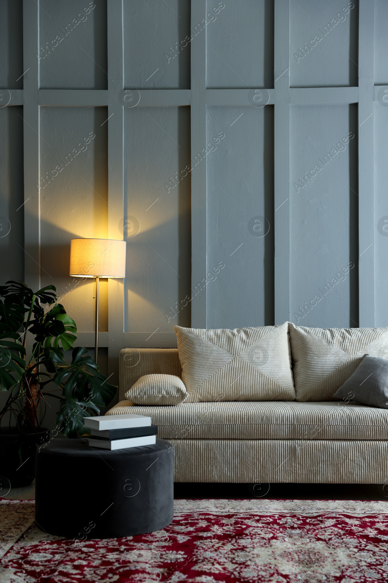 Photo of Comfortable sofa with pillows, lamp, houseplant and pouf near grey wall indoors. Space for text