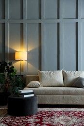 Photo of Comfortable sofa with pillows, lamp, houseplant and pouf near grey wall indoors. Space for text