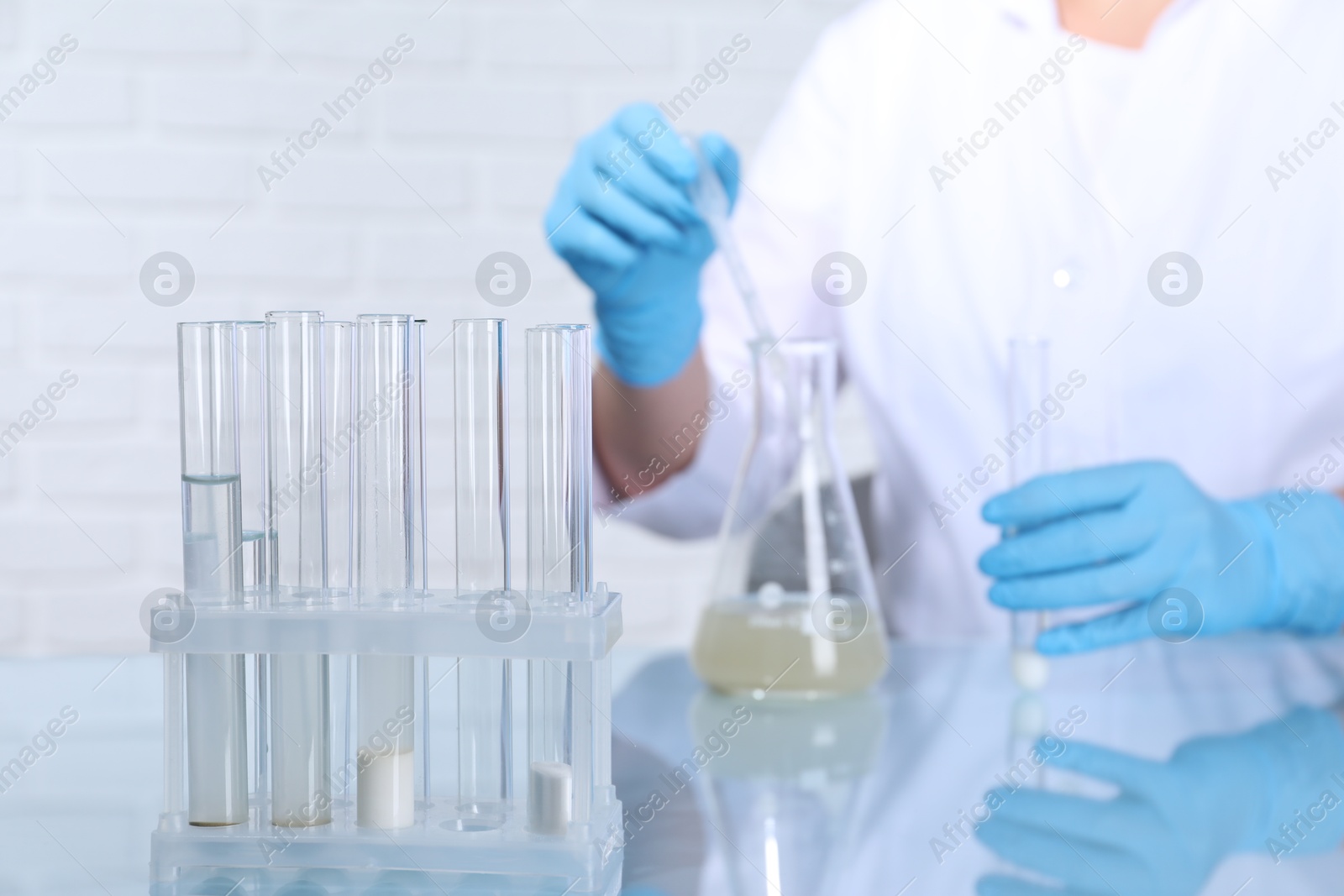 Photo of Laboratory testing. Scientist taking sample from flask at table indoors, focus on test tubes