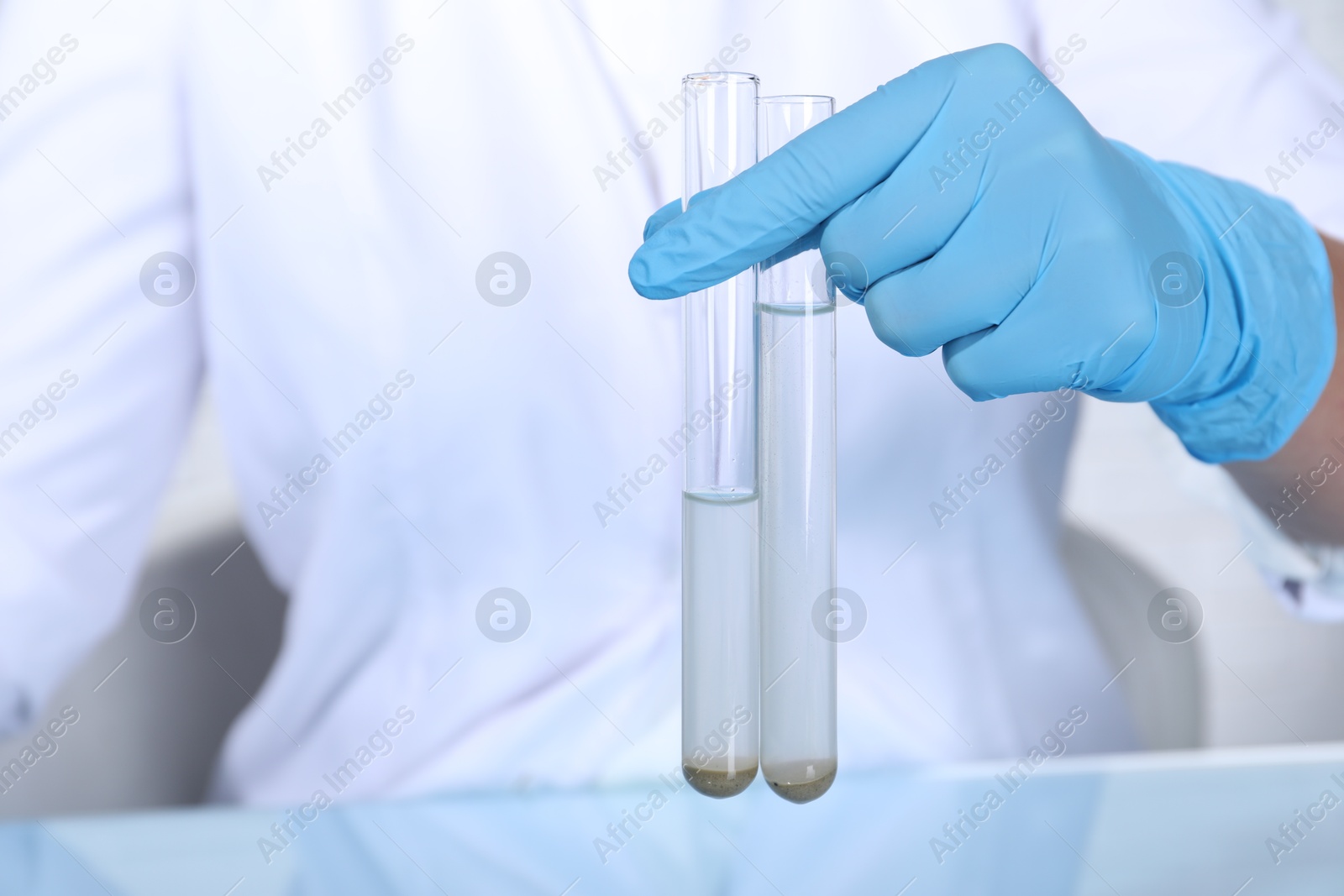 Photo of Laboratory testing. Scientist holding test tubes with samples at table indoors, closeup