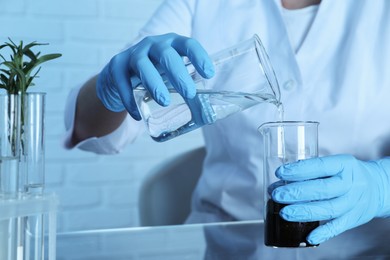 Photo of Laboratory testing. Scientist pouring liquid into beaker at table indoors, closeup