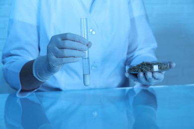 Photo of Laboratory testing. Scientist holding test tube of liquid and petri dish with sand sample at table indoors, closeup