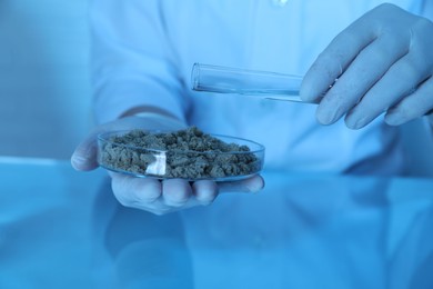 Photo of Laboratory testing. Scientist pouring liquid onto sand sample at table indoors, closeup