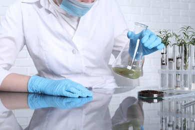 Photo of Laboratory testing. Scientist holding flask with sample at table indoors, closeup