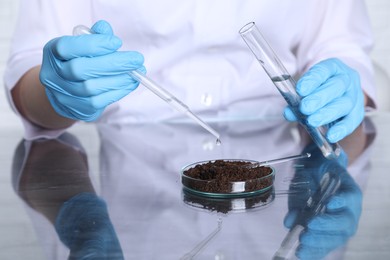 Photo of Laboratory testing. Scientist with test tube dripping liquid onto soil sample at table, closeup