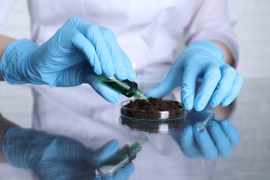 Photo of Laboratory testing. Scientist dripping liquid onto soil sample at table indoors, closeup