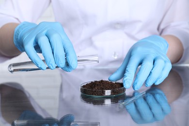 Photo of Laboratory testing. Scientist pouring liquid onto soil sample at table indoors, closeup