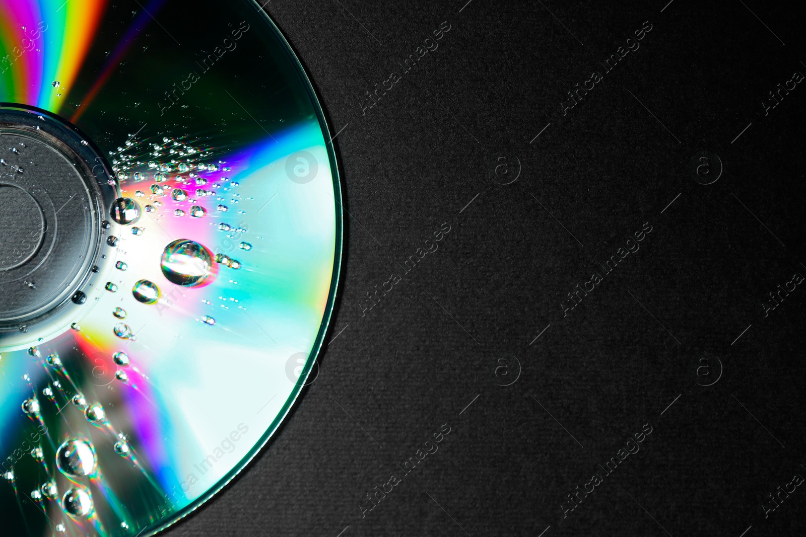 Photo of Compact disc with drops on black background, top view. Space for text