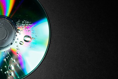 Photo of Compact disc with drops on black background, top view. Space for text