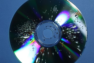 Photo of Compact disc with drops on blue background, top view