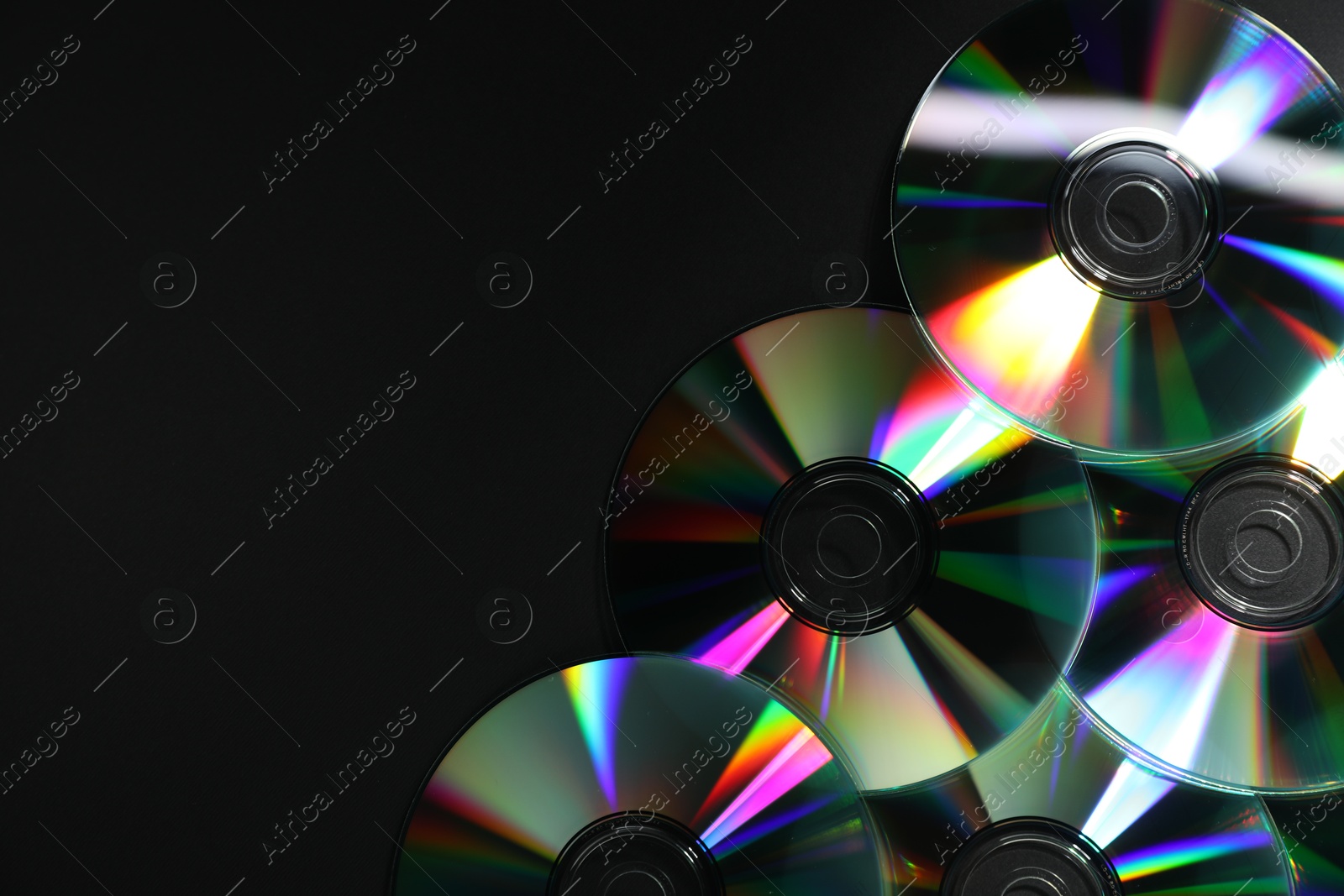 Photo of Shiny compact discs on black background, top view. Space for text