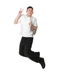 Teenage boy with backpack jumping and showing V-sign on white background