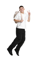 Teenage boy with backpack jumping and showing V-sign on white background