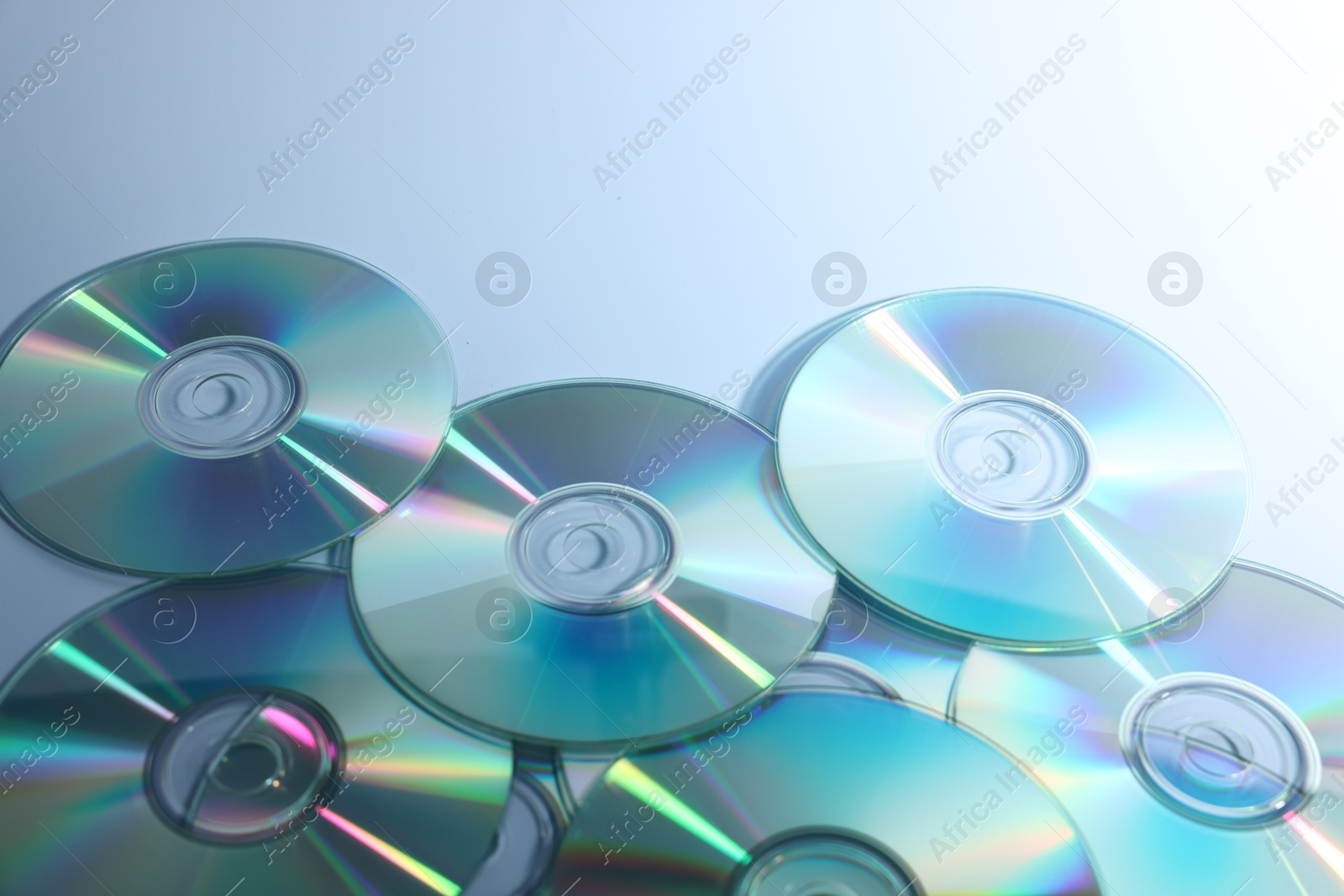 Photo of Many shiny compact discs on dusty blue background, closeup