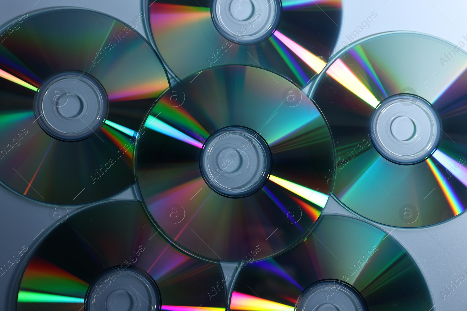 Photo of Many shiny compact discs on dusty blue background, flat lay