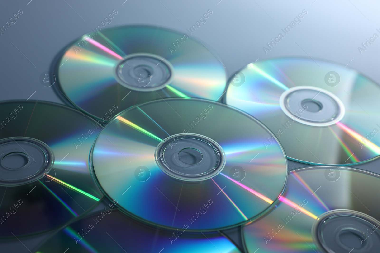 Photo of Many shiny compact discs on dusty blue background, closeup