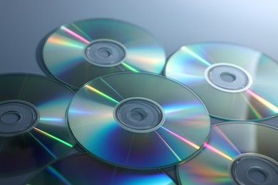 Photo of Many shiny compact discs on dusty blue background, closeup