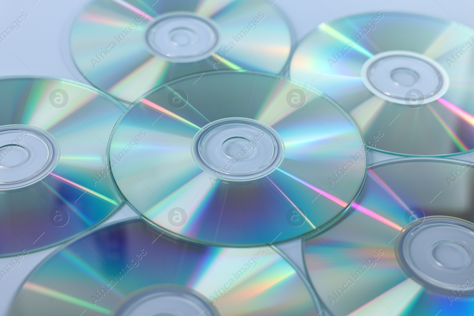 Photo of Many shiny compact discs on dusty blue background, closeup