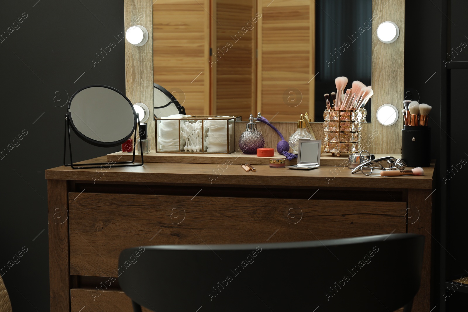 Photo of Makeup room. Wooden dresser with mirrors, different beauty products and chair indoors