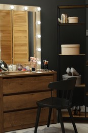 Photo of Makeup room. Wooden dresser with mirror, different beauty products, chair and shoes indoors