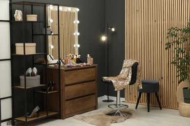 Photo of Makeup room. Wooden dresser with mirror, different beauty products, chair and shoes indoors