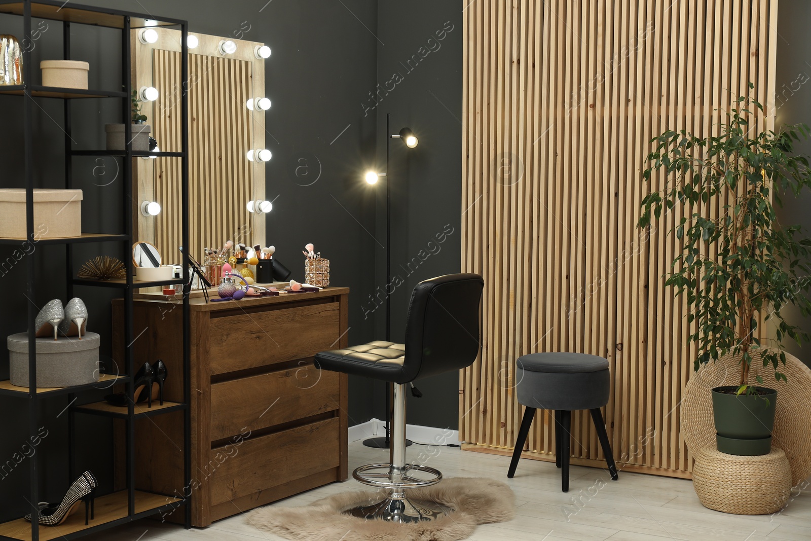 Photo of Makeup room. Wooden dresser with mirror, different beauty products, shoes, houseplant and chair indoors