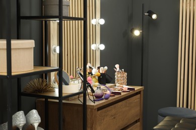 Photo of Makeup room. Wooden dressing table with mirror, different beauty products and lamp indoors