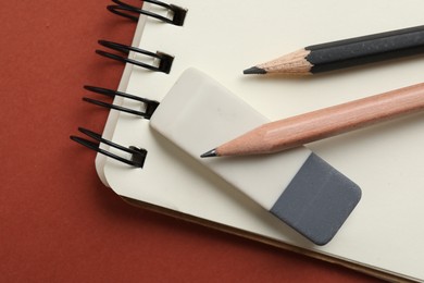 Photo of Eraser, pencils and notebook on brown background, top view