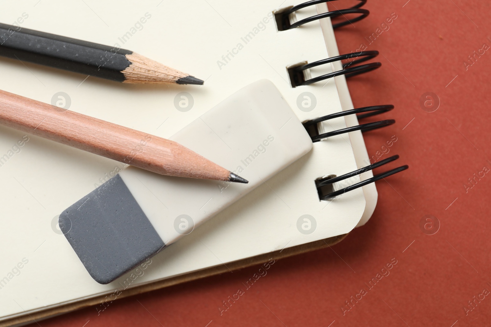 Photo of Eraser, pencils and notebook on brown background, top view