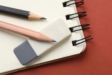 Photo of Eraser, pencils and notebook on brown background, top view