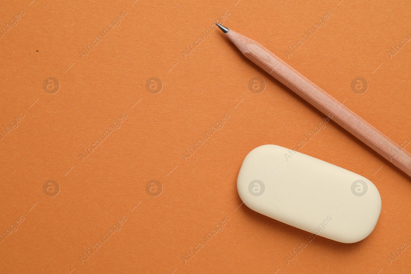 Photo of Eraser and pencil on orange background, flat lay. Space for text