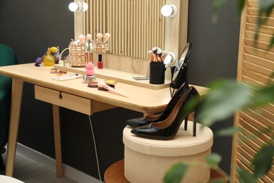 Photo of Makeup room. Wooden dressing table with mirror, different beauty products and shoes indoors