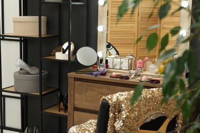 Photo of Makeup room. Wooden dressing table with mirror, different beauty products, shoes and chair indoors